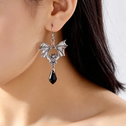 Silver bat dangle earrings with black teardrop drop, worn close-up on ear