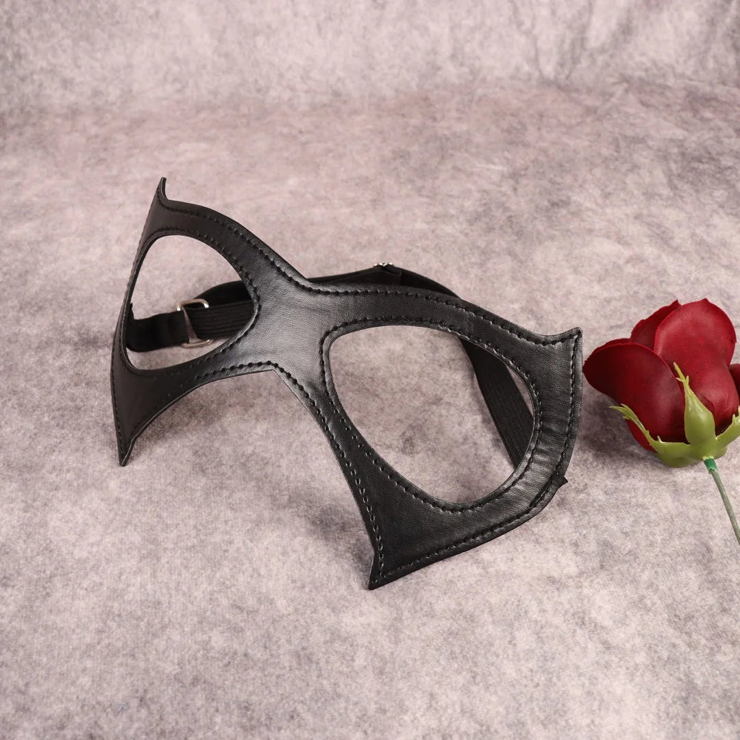 Black cat-eye mask with curved eye openings, visible stitching, elastic strap, flat lay