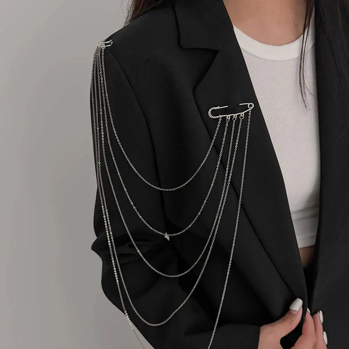 Layered silver chain drape necklace over a dark blazer with clasp at the collar