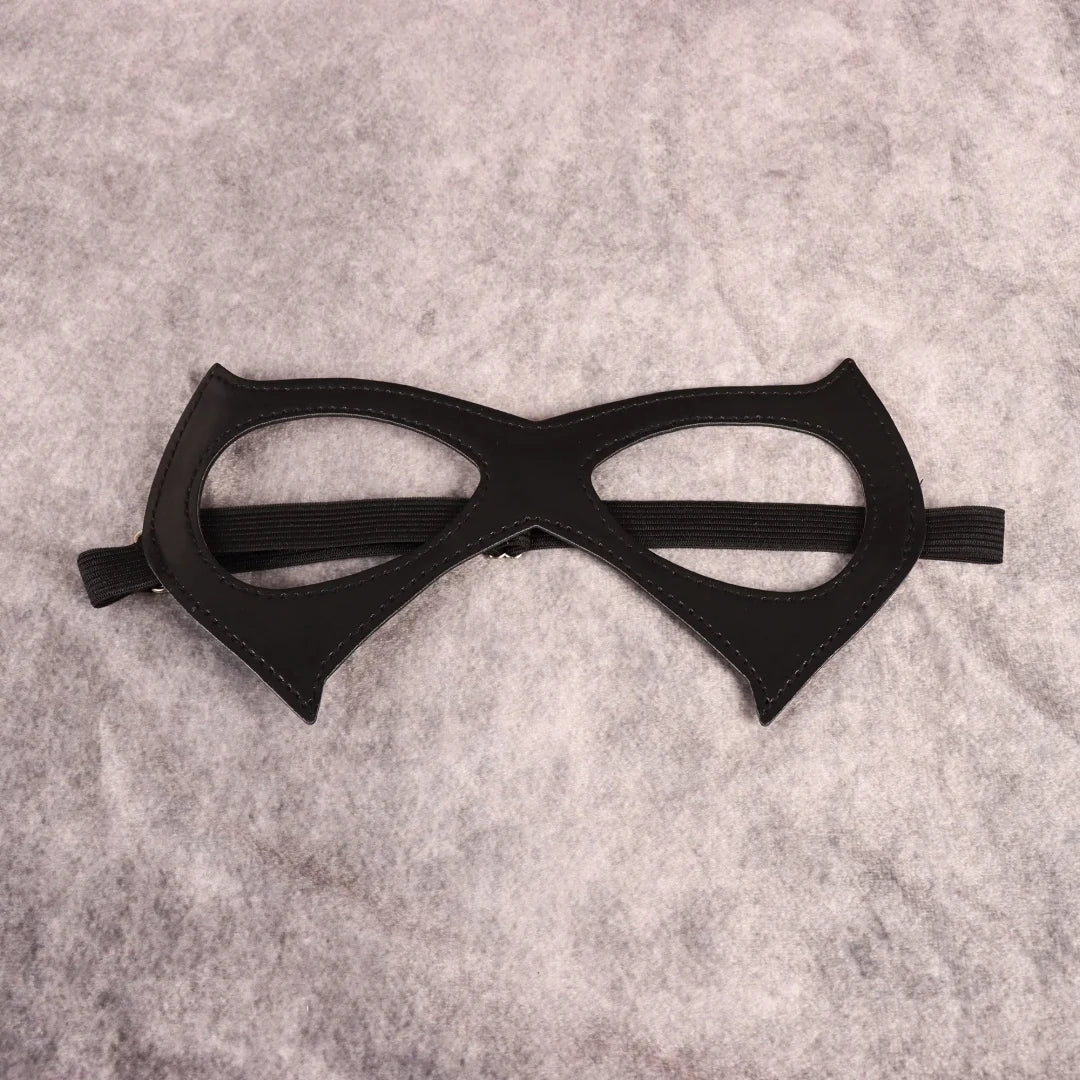 Black cat-eye mask with open eye cutouts, pointed cheek panels, elastic band, flat lay