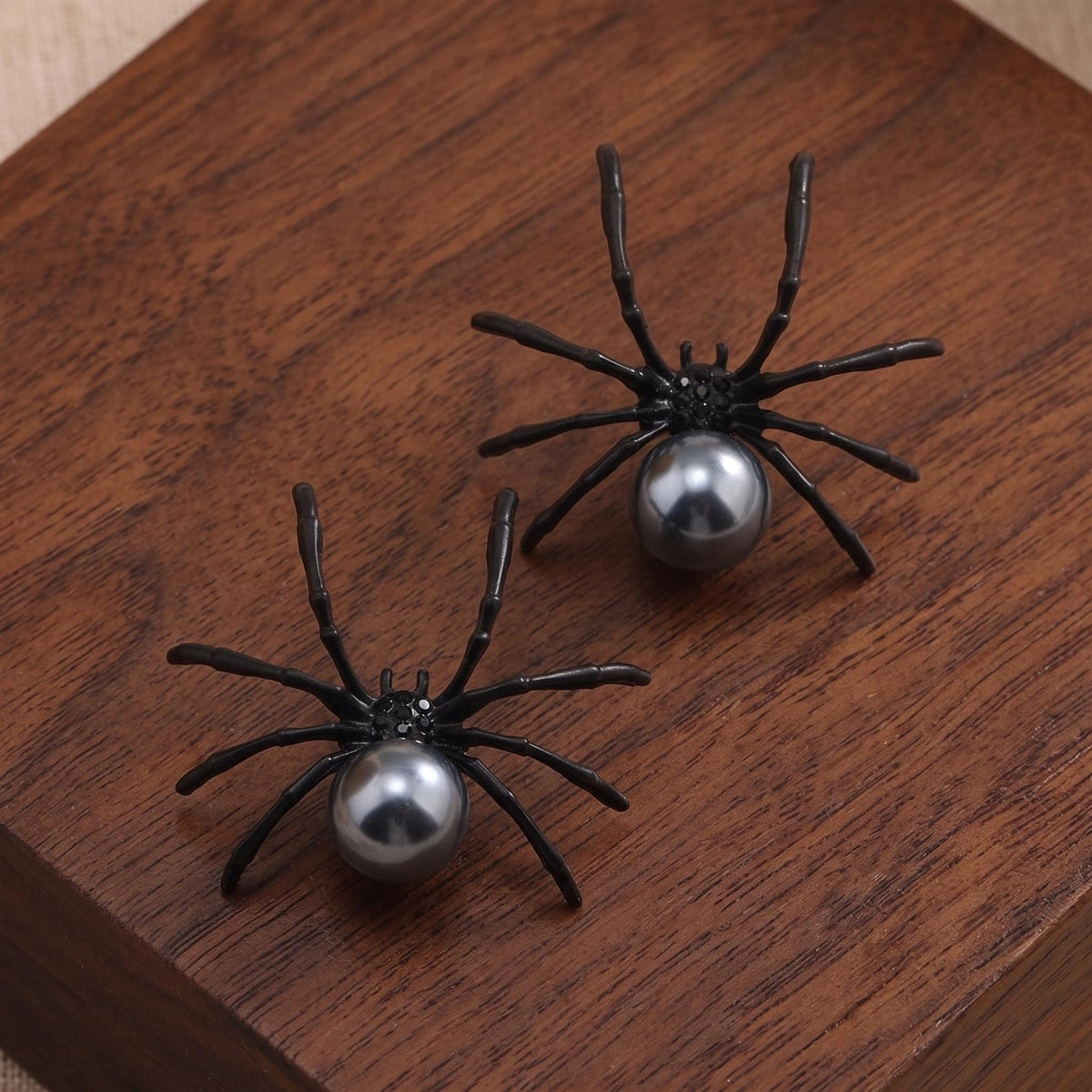 Two black spider pearl earrings with round gray bead on display